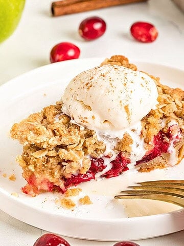 Crumble and ice cream topped apple cranberry pie on a white plate.
