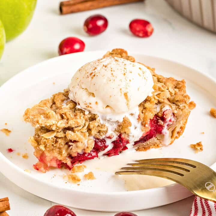 Crumble and ice cream topped apple cranberry pie on a white plate.