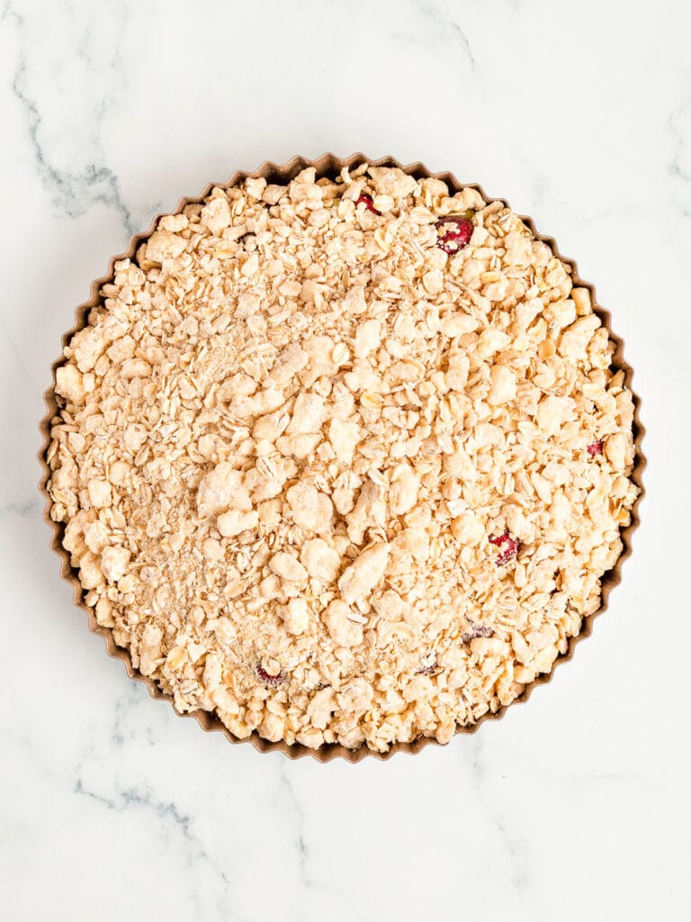 Crumble-topped pie in a metal pan before baking. White marble surface.