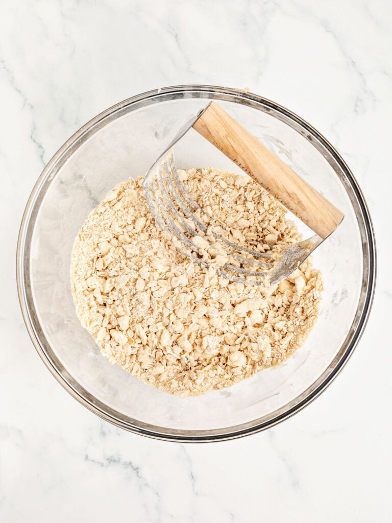 Crumb topping in a glass bowl with a pastry cutter. Marble surface.