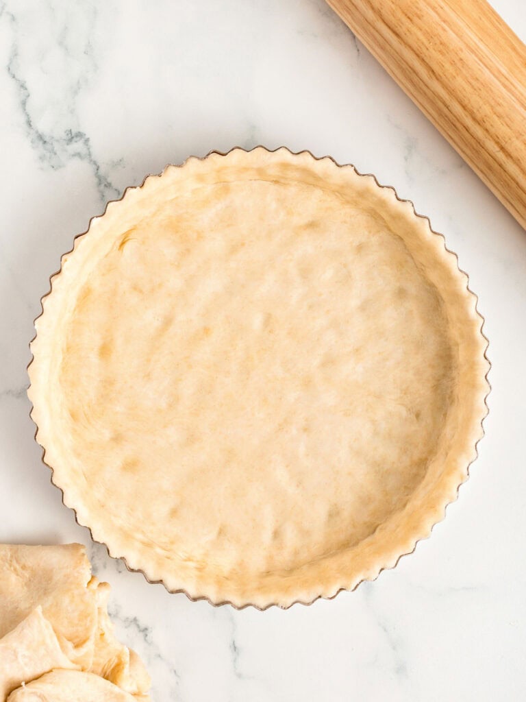 Pie crust lined metal pan on a white marble surface.