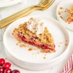 Cream-topped slice of apple cranberry streusel pie on a white plate. Gold forks.