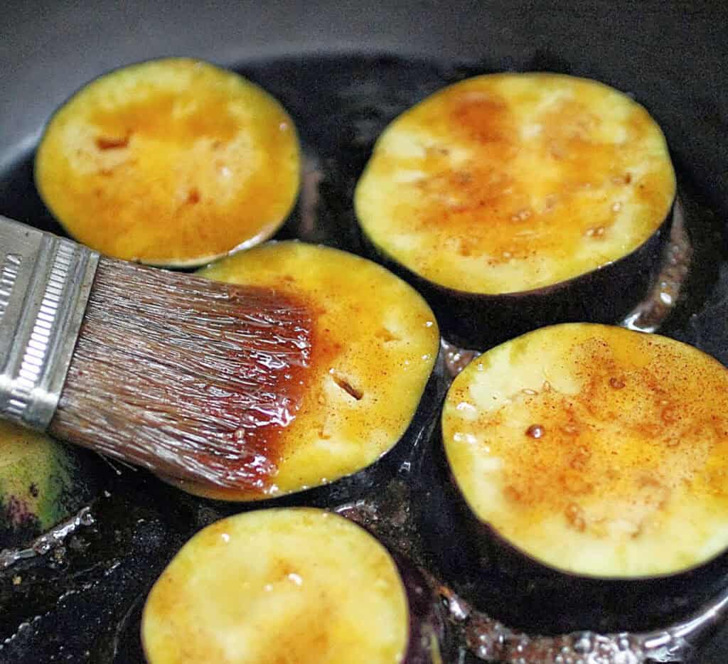 Brushing honey mixture over eggplant rounds in a black skillet.
