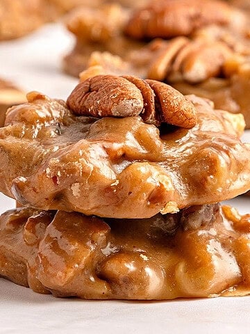 Two pecan pralines stacked on white paper.