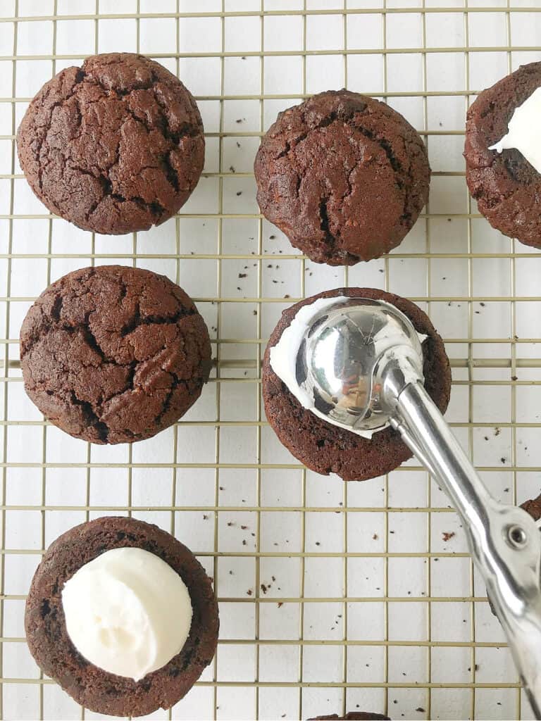 Scooping cream cheese filling on chocolate whoopie pie half on a wire rack.
