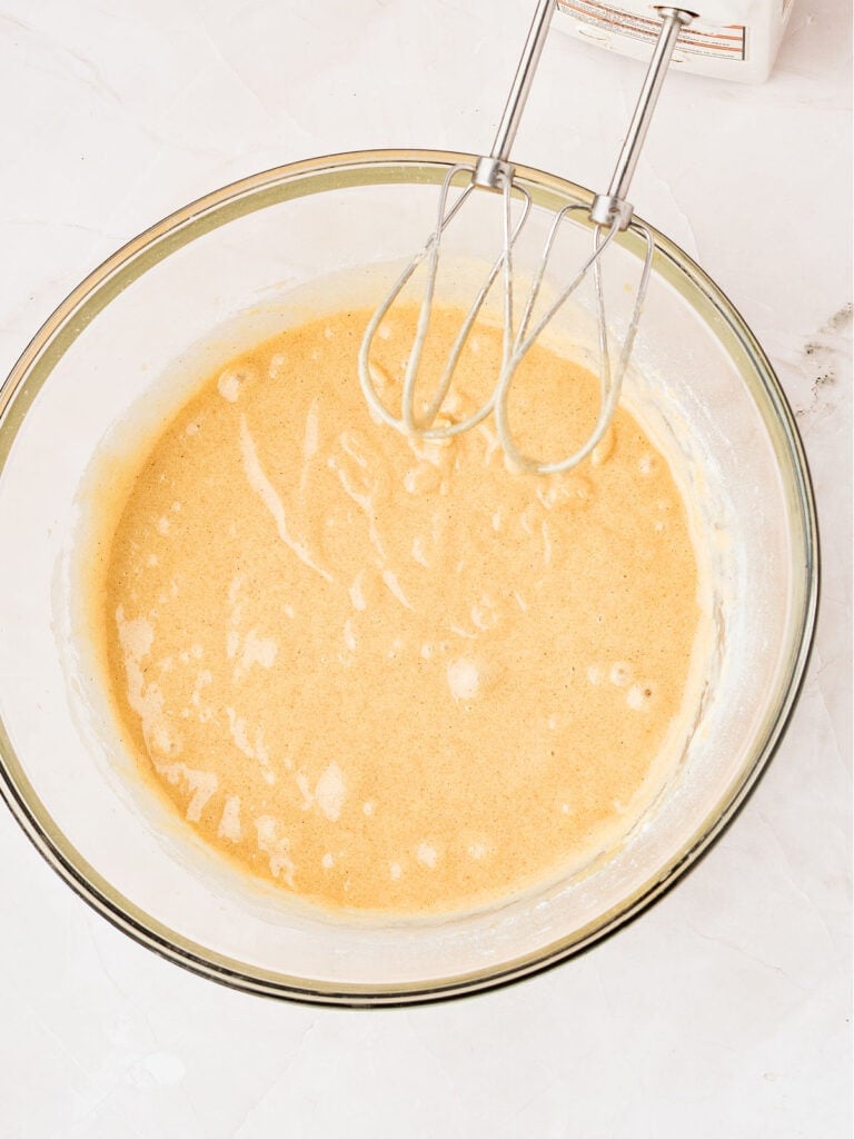 Glass bowl with cake batter and beaters. White background.