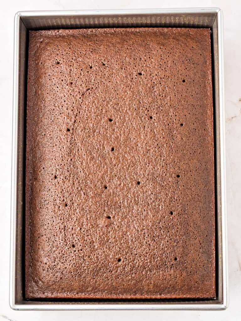 Poked baked chocolate cake in a rectangular metal pan.