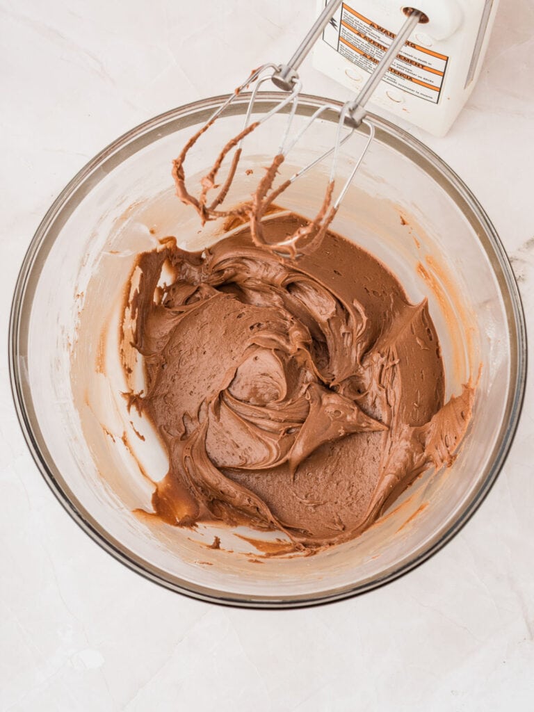 Chocolate frosting in a glass bowl with electric beaters. White surface.