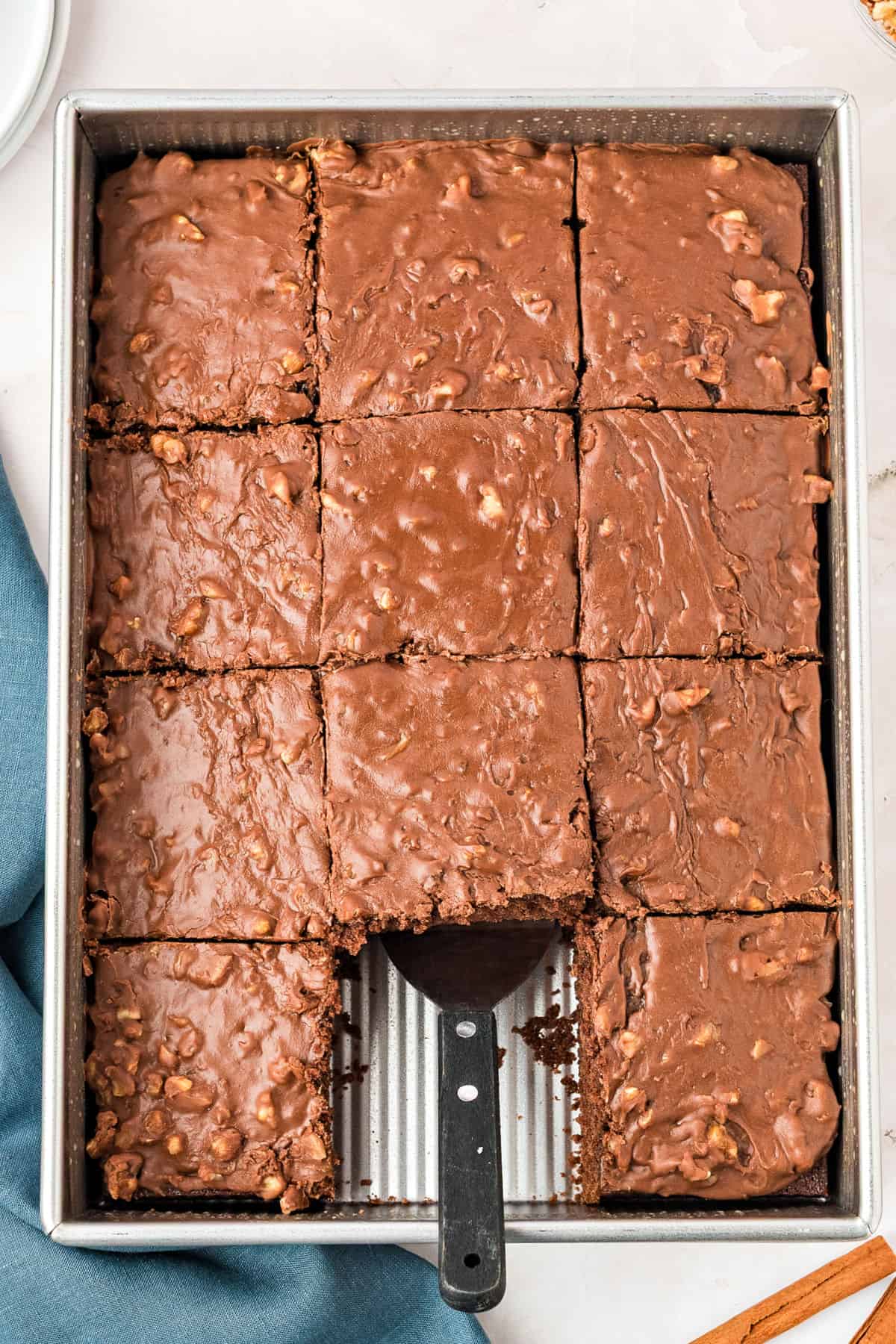 Chocolate walnut sheet cake in a metal pan with a spatula. Square missing.