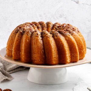 Whole rum bundt cake on a white cake stand. White background.