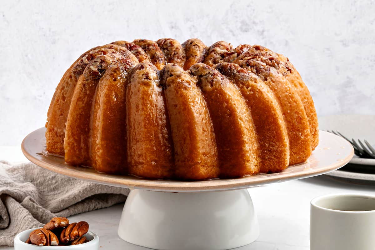 Horizontal image of white cake stand with rum pecan bundt cake.