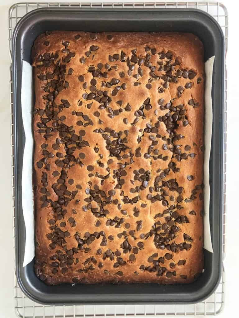Baked chocolate chip cake in a rectangular dark metal pan on a wire rack.