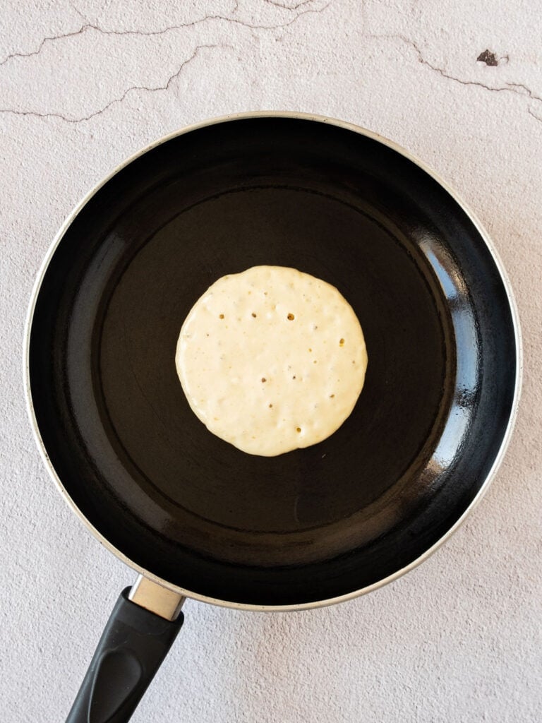Half-cooked pancake on a black skillet on a light gray surface.