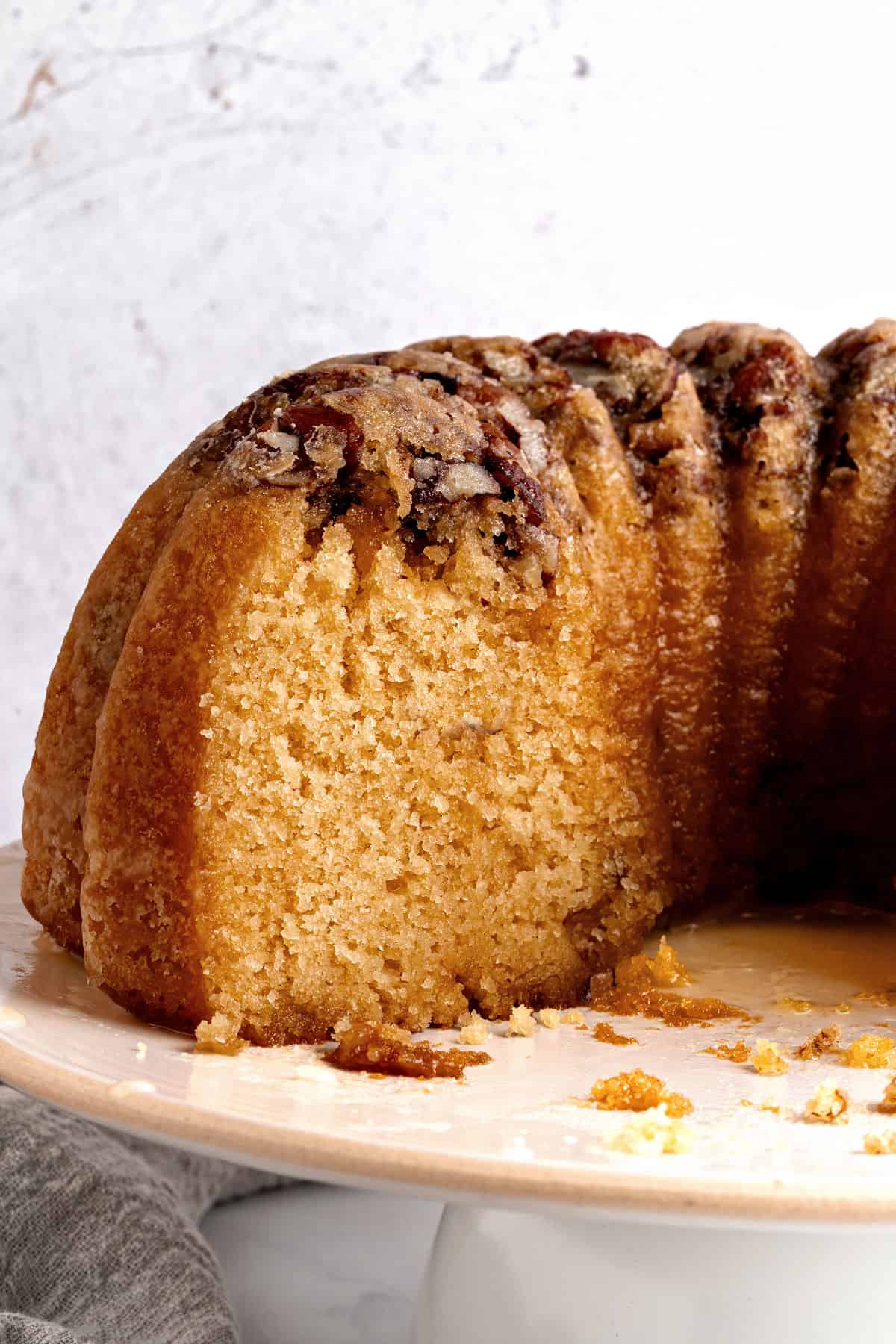 Cut rum pecan bundt cake on a white cake stand.
