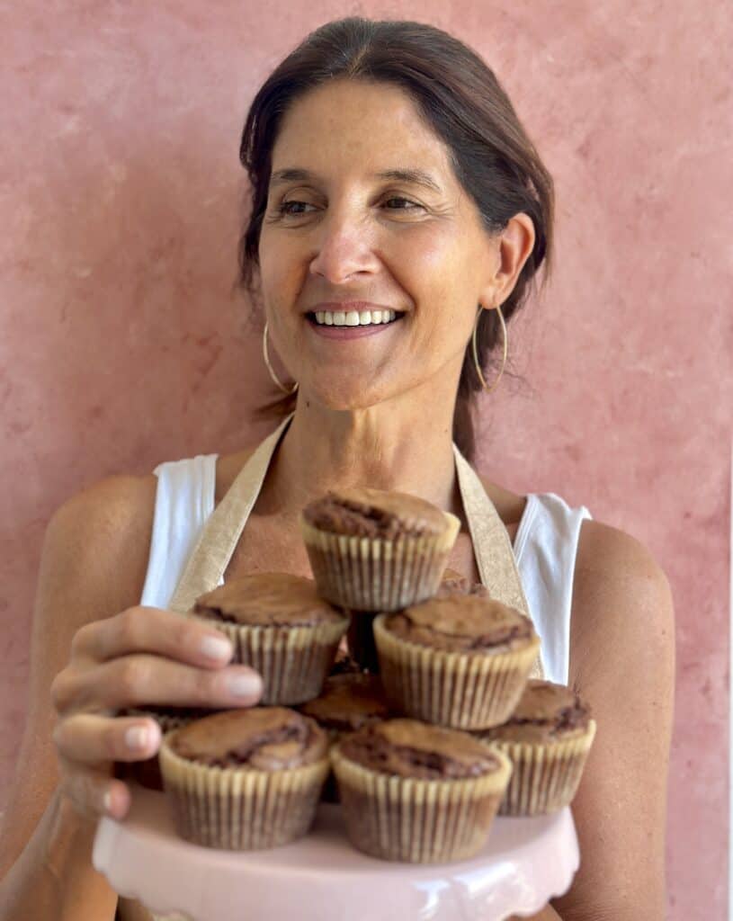 Paula with a tray of brownie muffins. Pink backdrop.