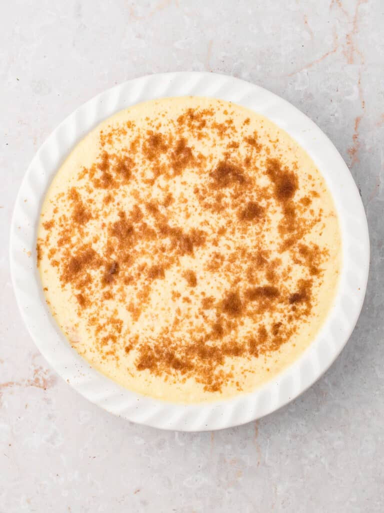 Round ceramic pie dish with crustless coconut pie batter. Gray background.
