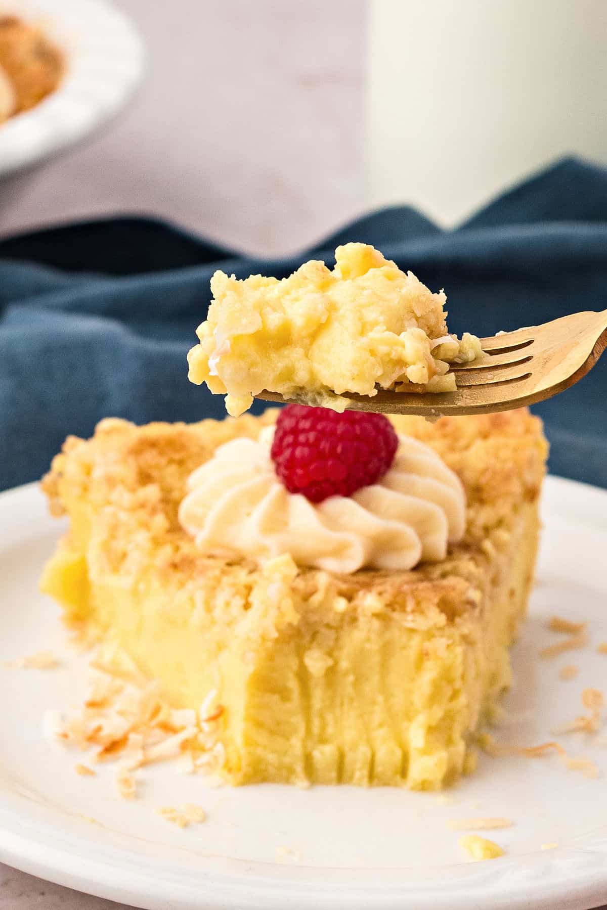 Gold fork with bite of crustless coconut pie. White plate, blue towel.