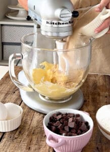 Stand mixer, bowls with ingredients, wooden surface.