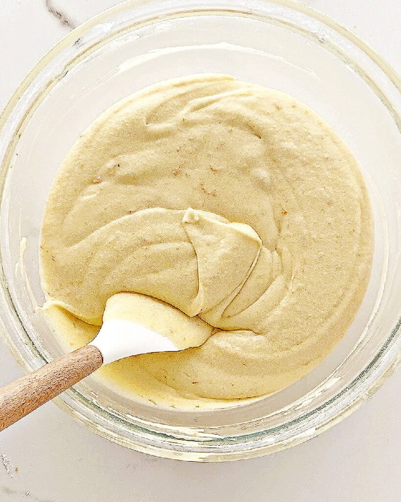 Vanilla cake batter in a glass bowl. White wood spatula.