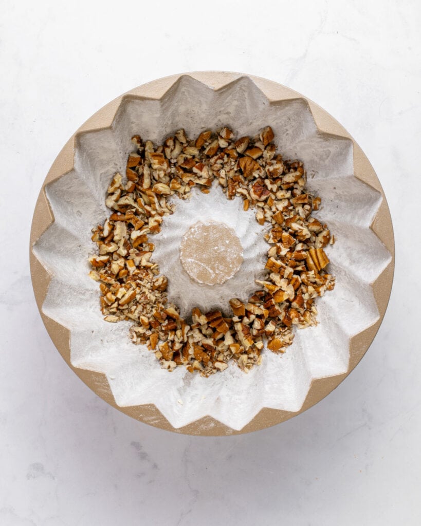 Floured bundt pan with chopped pecans. White background.
