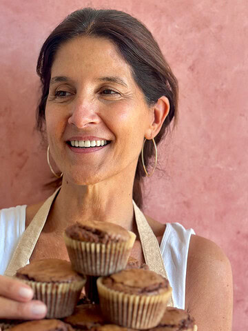 Smiling Paula with a tray of brownie muffins. Pink background.