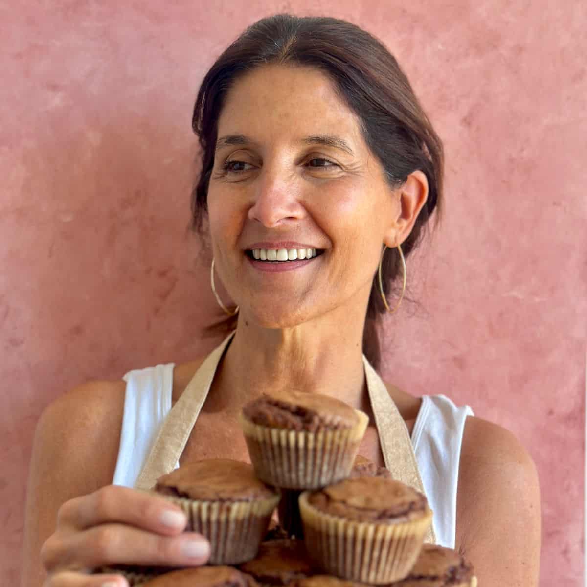 Smiling Paula with a tray of brownie muffins. Pink background.