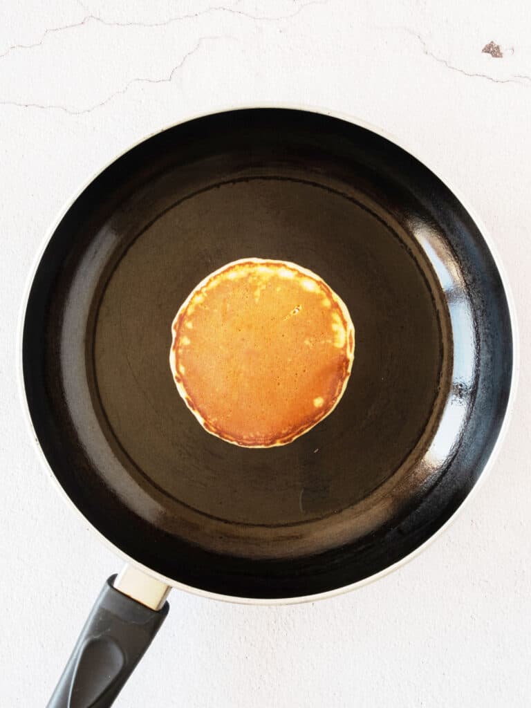Cooked pancake on a black skillet. White surface.