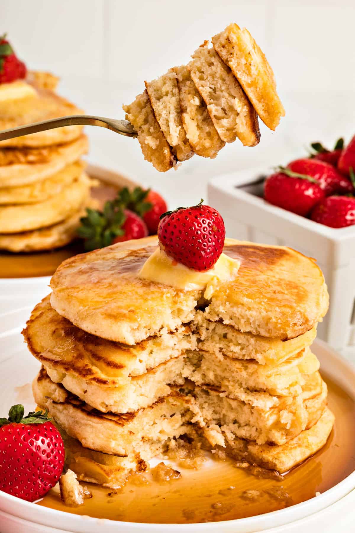 Ricotta pancake stack cut and forked. White plate, syrup and strawberries.