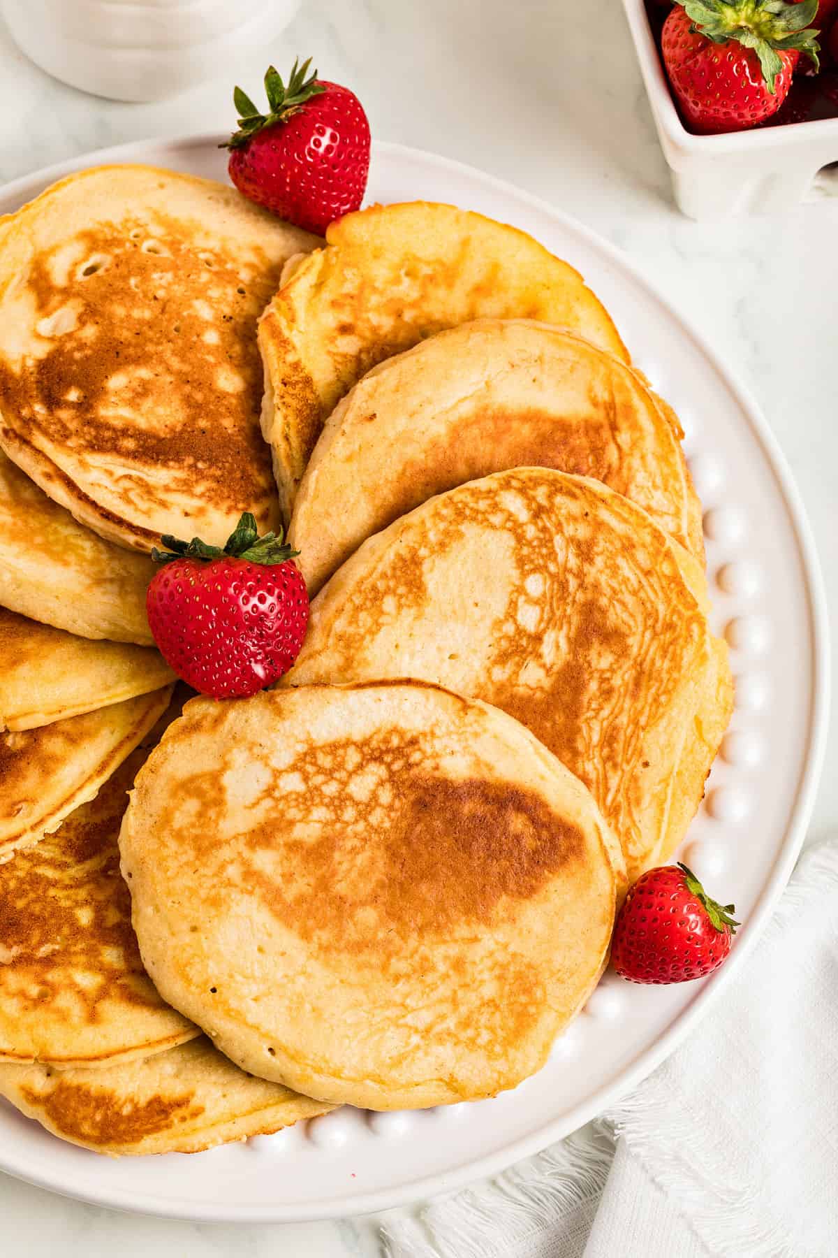 Overlapping ricotta pancakes on a white platter. Fresh strawberries.
