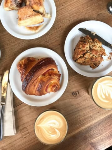 Wooden surface with croissant and scone on white plates. Coffee cups. 