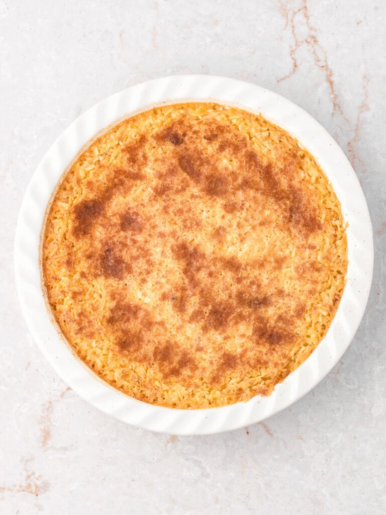 Baked crustless coconut pie in a white ceramic dish. Gray surface.