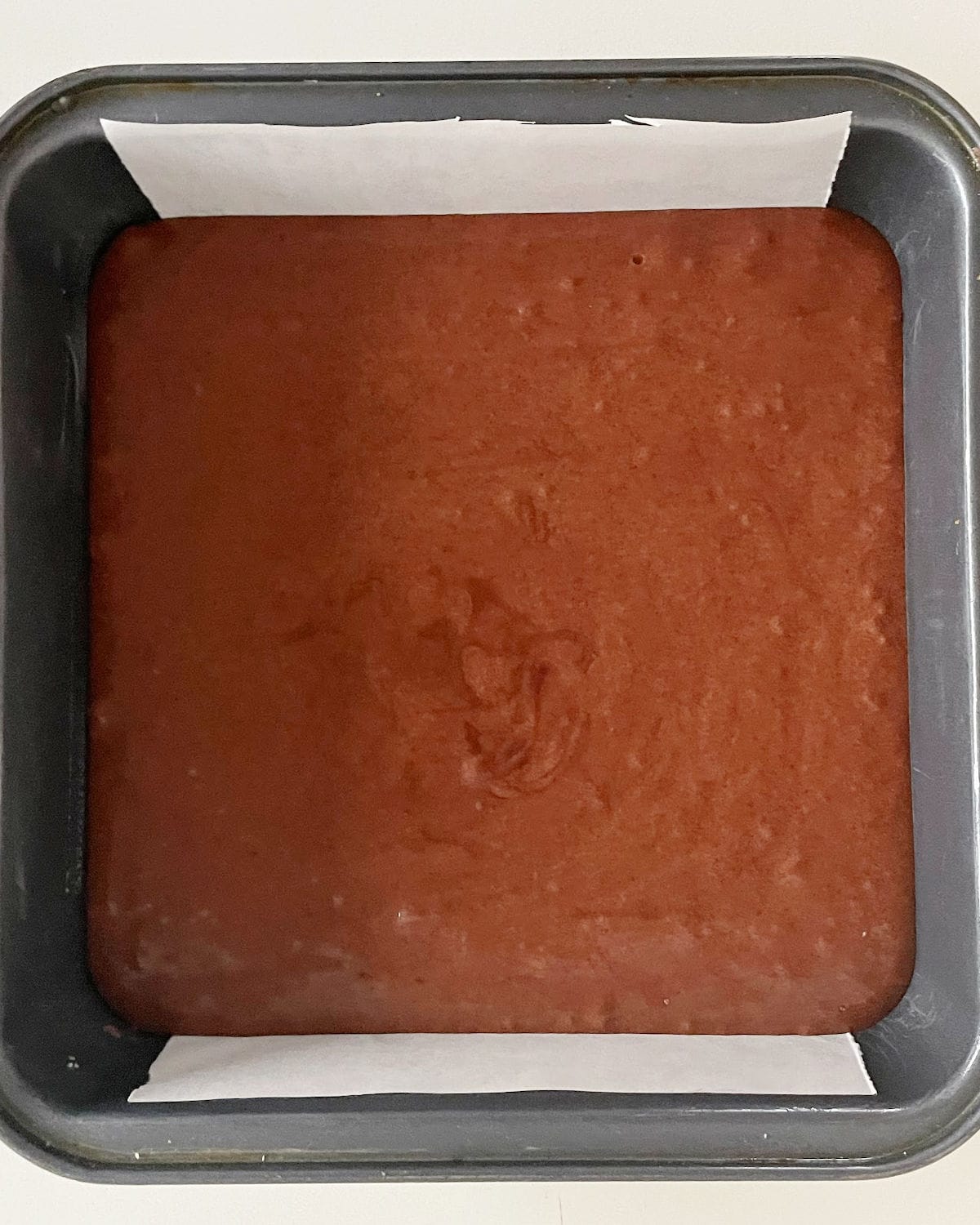Square pan with brownie batter on a whitish surface.