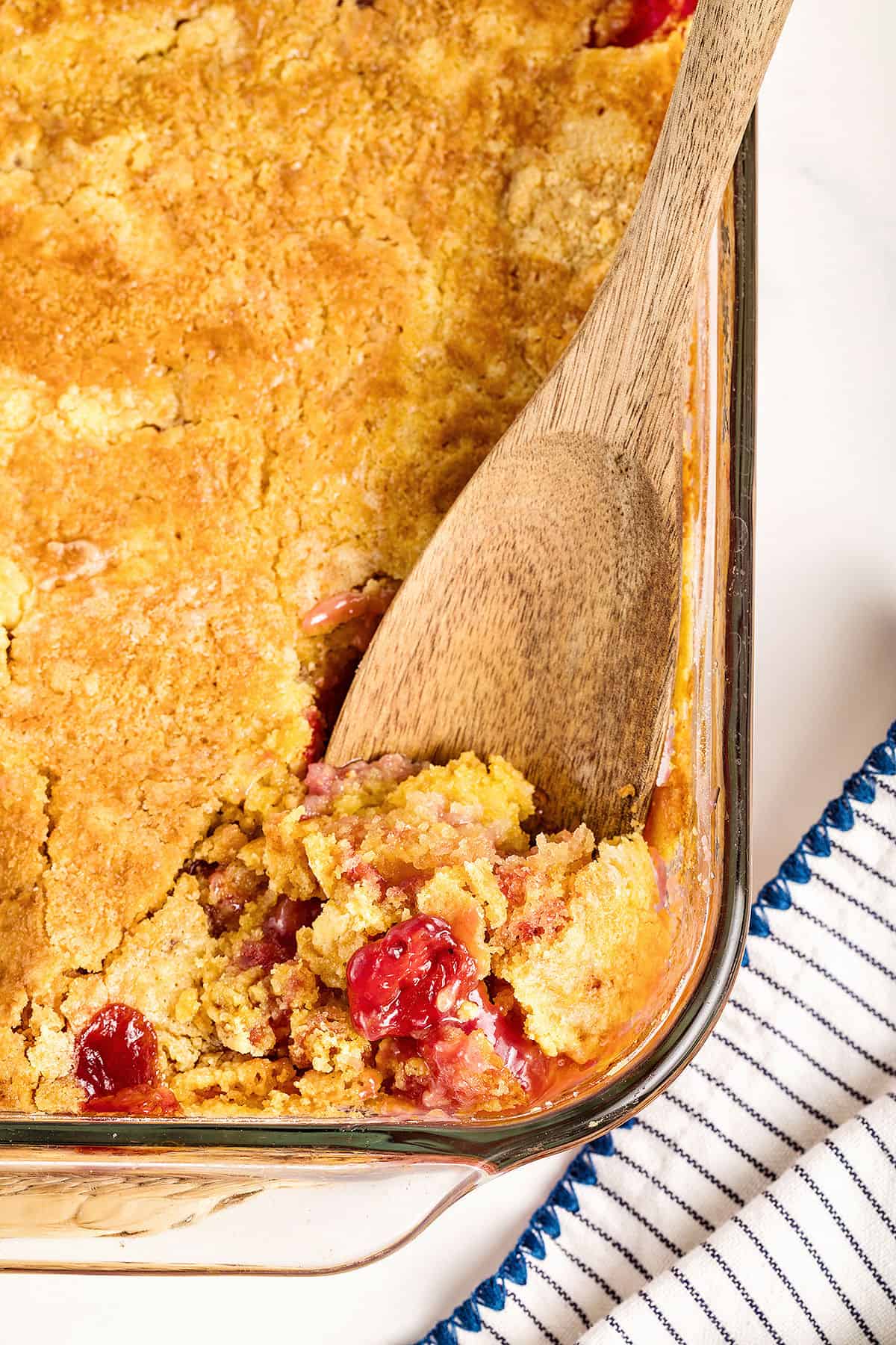 Glass dish of cherry pineapple dump cake. Wooden spoon.