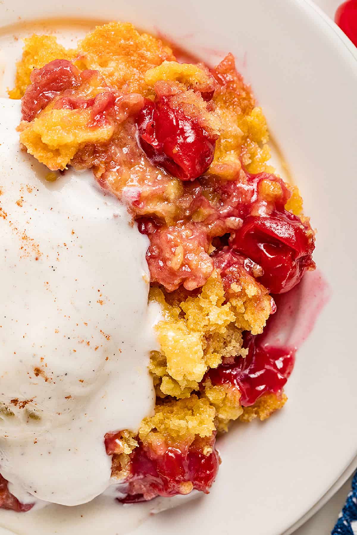 Close up portion of cherry pineapple cobbler with ice cream. White plate.