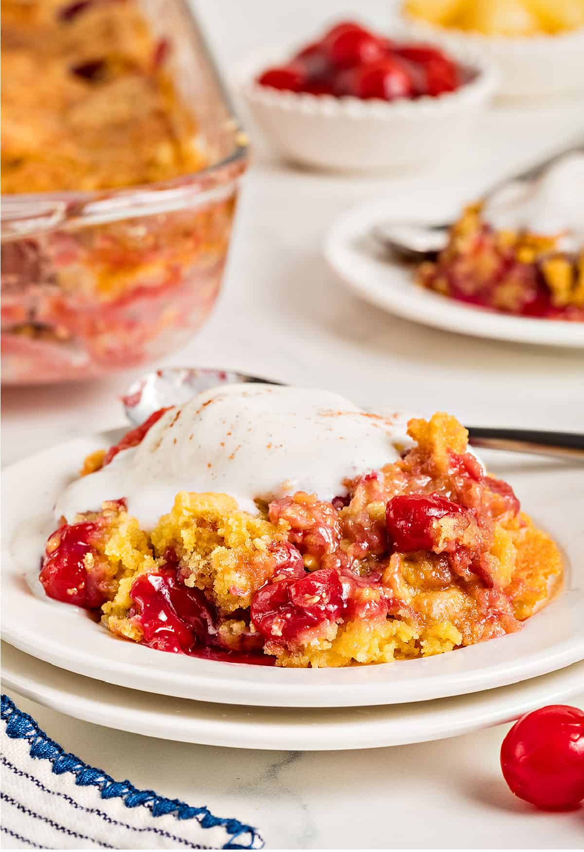 Pineapple cherry dump cake with ice cream. White plates, glass baking dish, white background.
