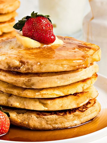 Close up stack of pancakes with syrup and fresh strawberries. White background.