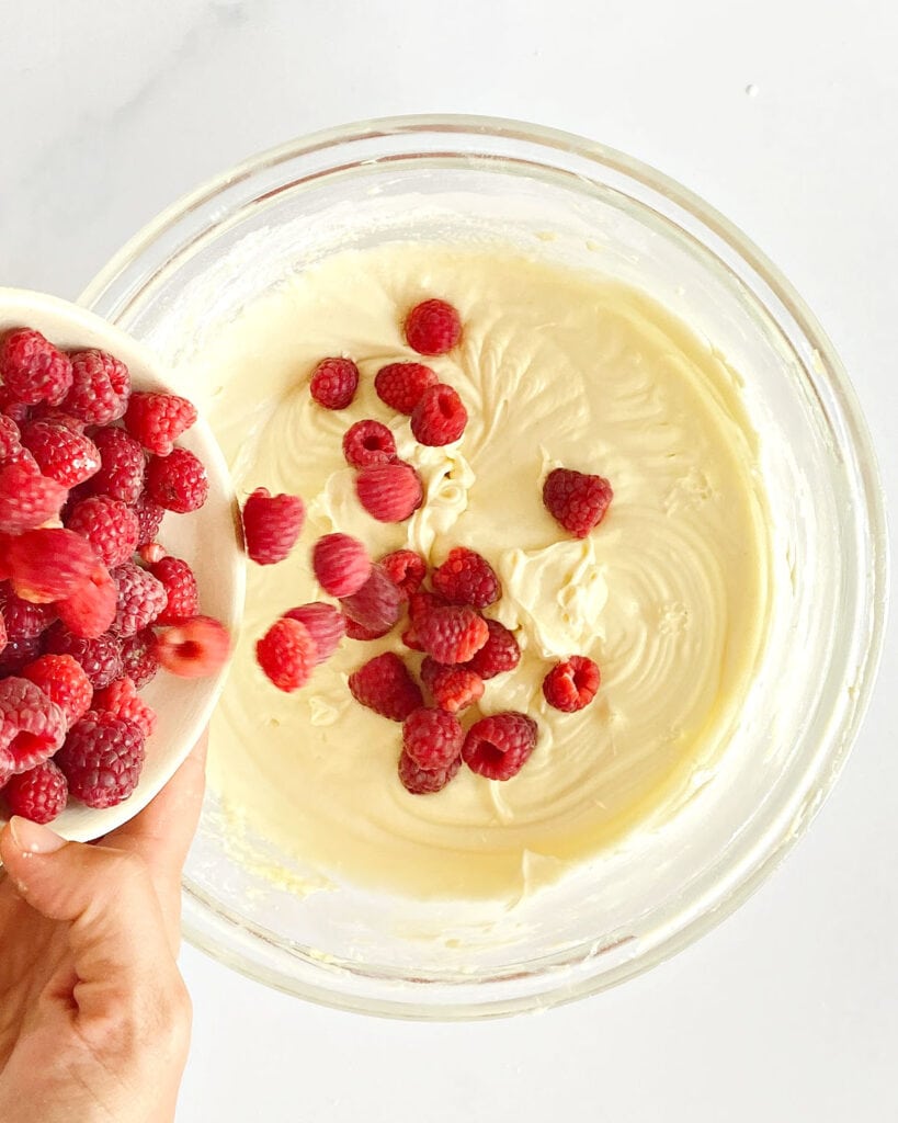 Adding fresh raspberries to white chocolate cake batter in a glass bowl.