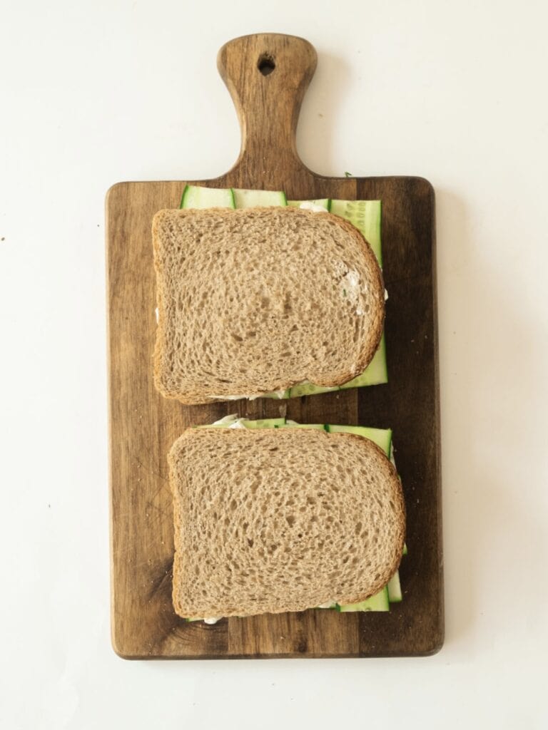 Assembled cream cheese cucumber sandwiches on a wooden board. White background.