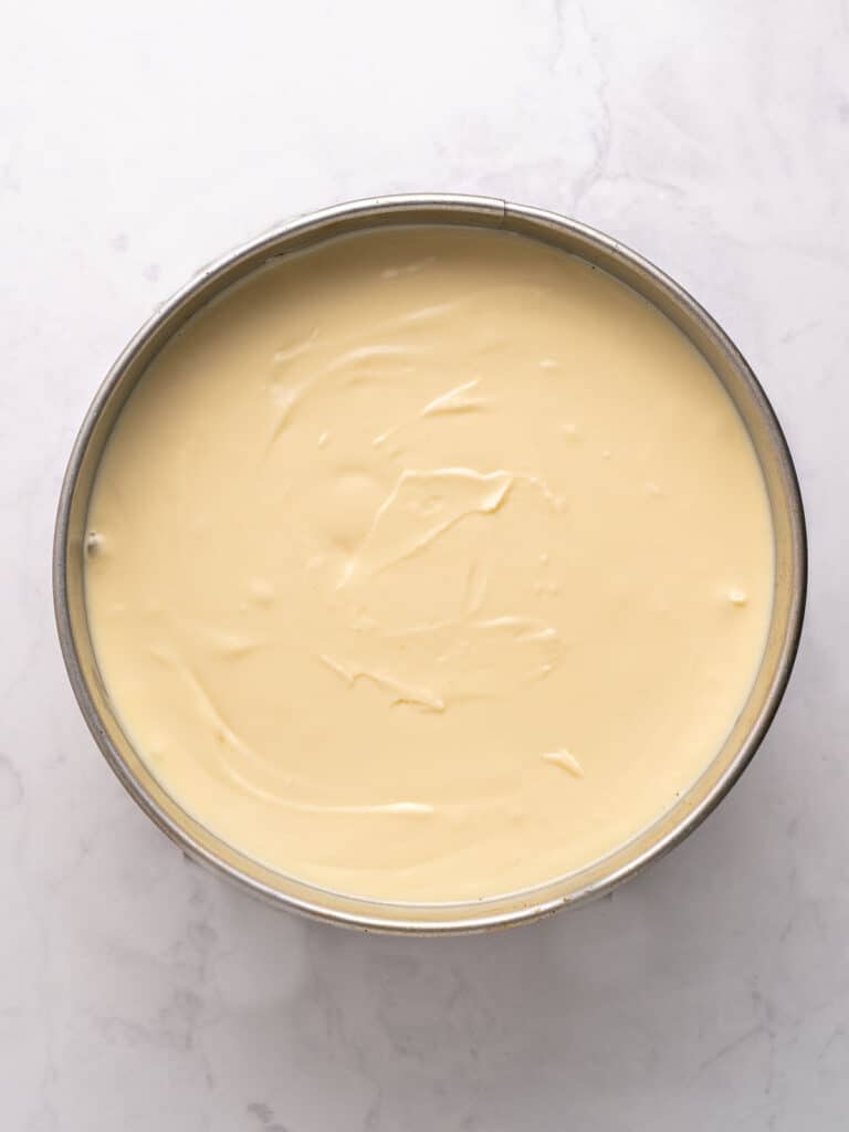 Cheesecake batter in a round metal cake pan. Light gray background.