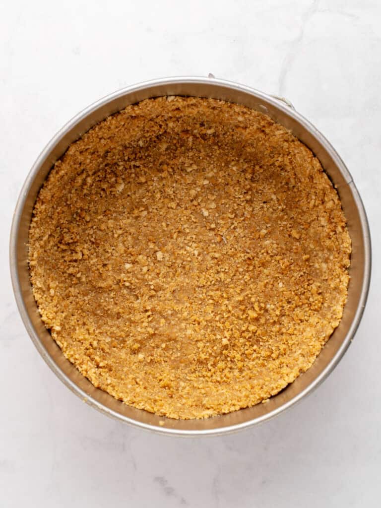 Crumb base for cheesecake in round metal pan. White background.