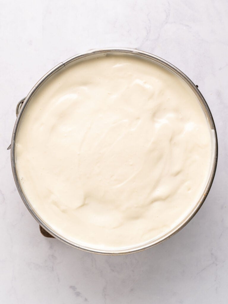 Round springform pan with sour cream topped cheesecake. Light gray background. 