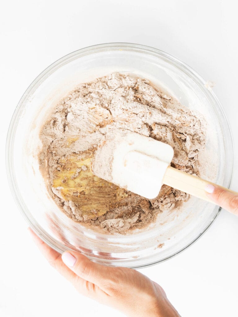 Mixing chocolate dough in a glass bowl with a white spatula. White background.