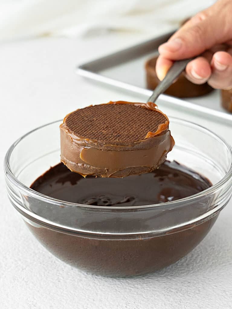 Dipping a dulce de leche alfajor into a glass bowl of melted chocolate. White background. 