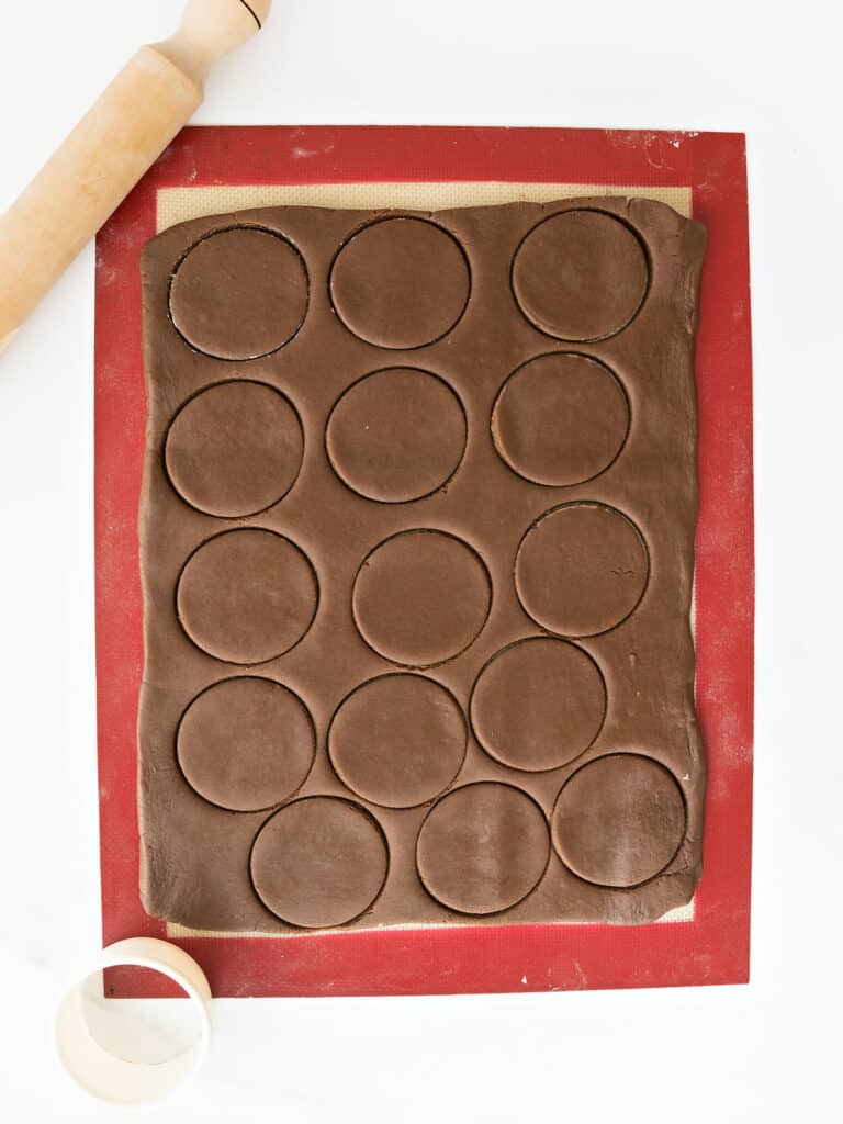 Silpat with rolled chocolate dough cut into rounds. Rolling pin and cutter.
