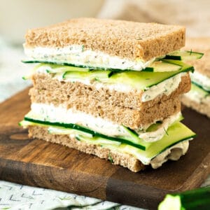 Wooden board with two cucumber cream cheese sandwich stack.