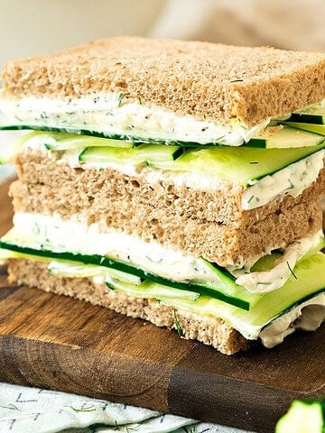 Wooden board with two cucumber cream cheese sandwich stack.