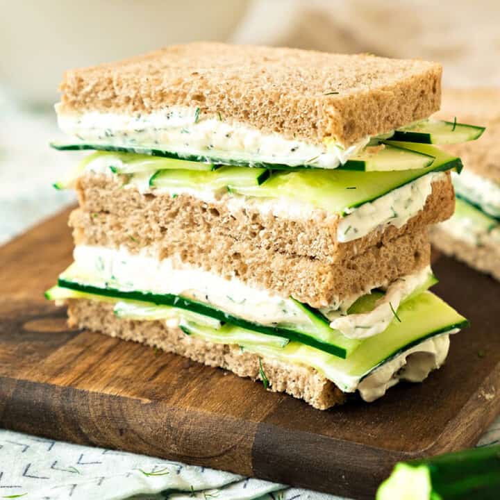 Wooden board with two cucumber cream cheese sandwich stack.