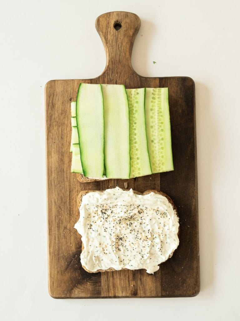 Assembling cucumber cream cheese sandwiches on a wooden board. White background.