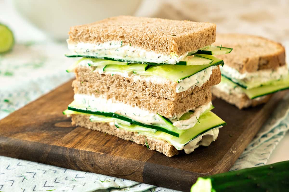 Horizontal image of wooden board with cucumber sandwiches.