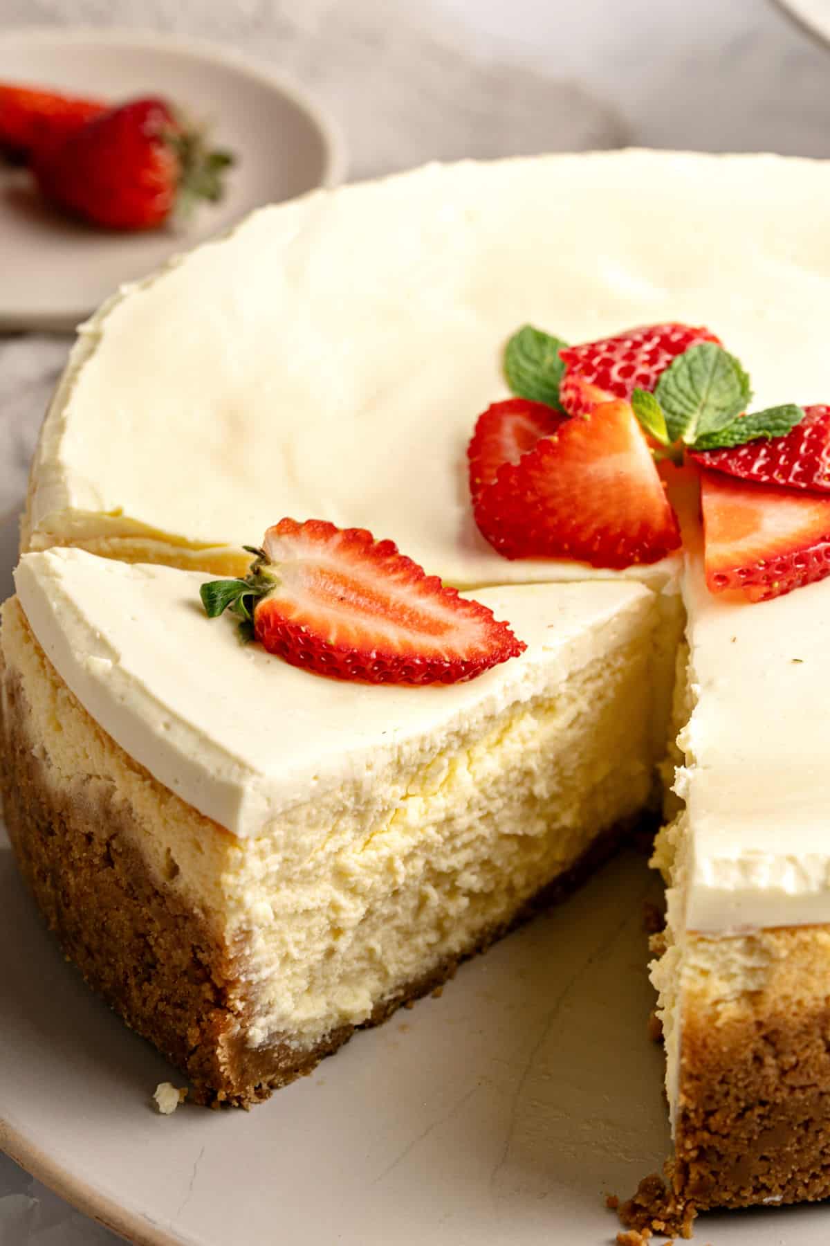 Cut slice of cheesecake with whole cake on a gray plate. Fresh strawberries.
